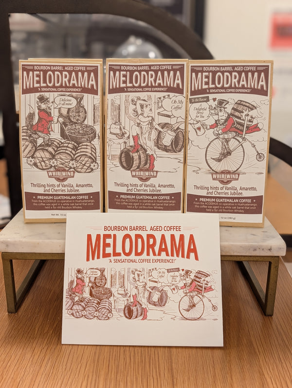 Three bags of Melodrama bourbon barrel aged coffee on a wooden surface.